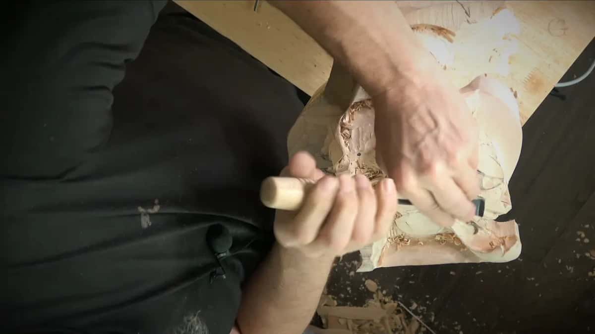 A gouge with a light handle cleans a lobe while the left hand steadies the big carved block