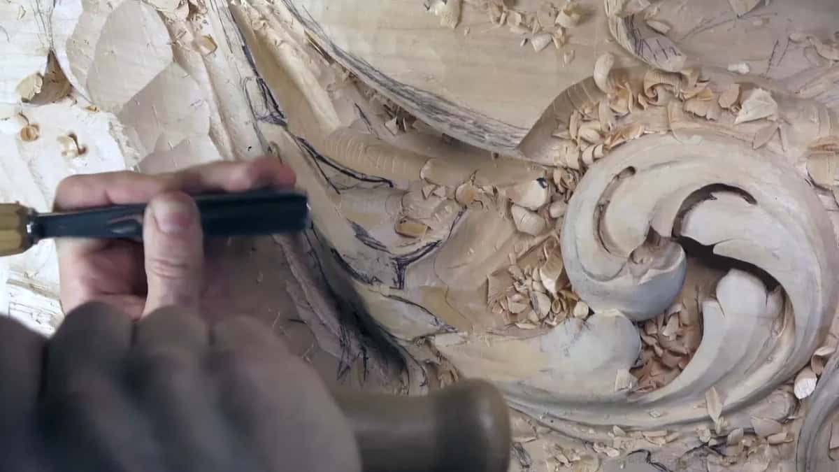 One fist grips a mallet while the other hand sets a black-handled gouge beside the scroll.