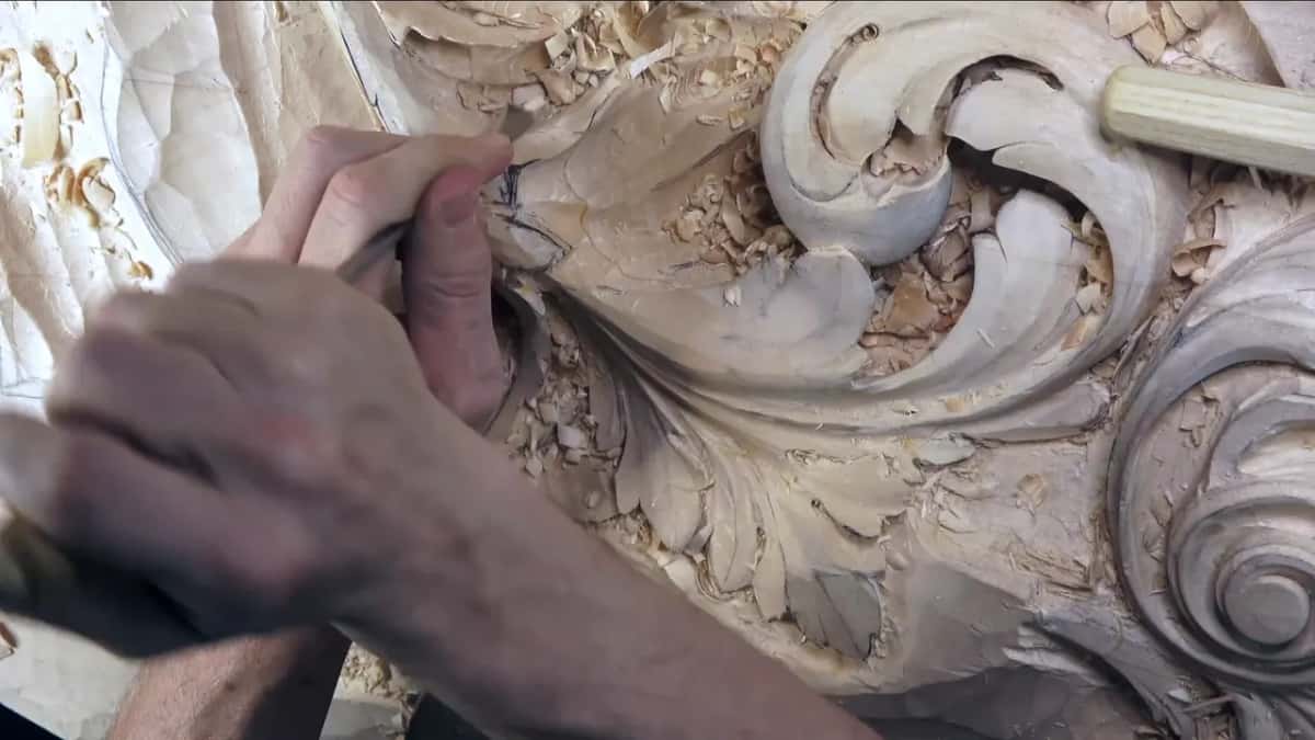 Knuckles grip a gouge near the top of a scroll.