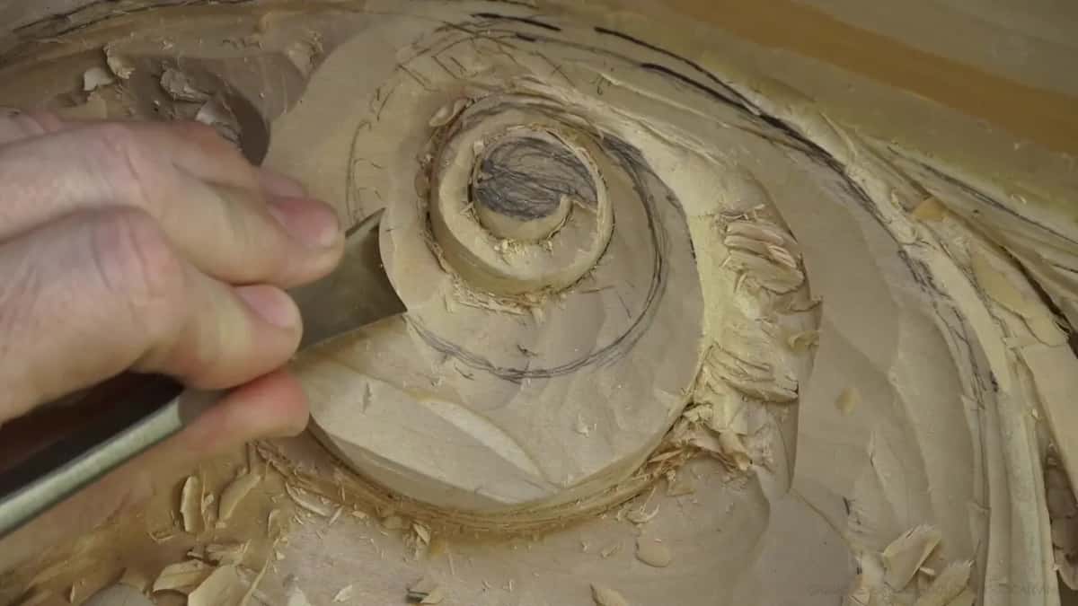 Fingers guiding a gouge round the roll of a volute drawn in pencil