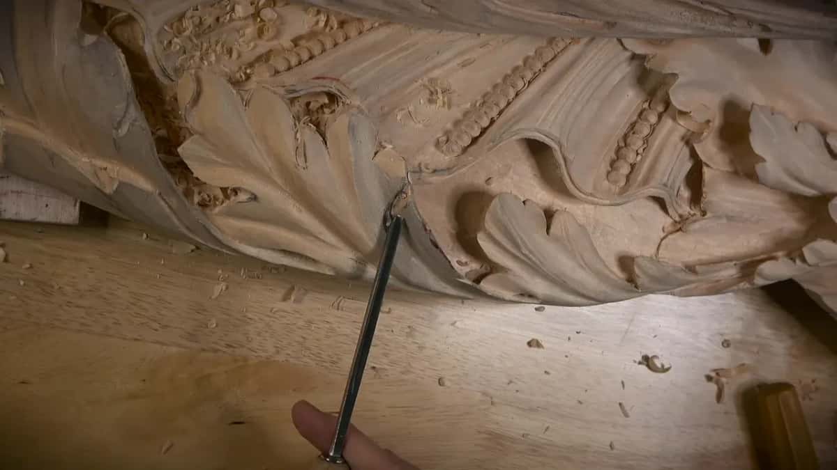 A long slim tool held from below, its tip under the edge of a carved leaf