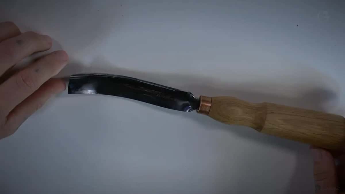 Both hands holding the long bent gouge flat on white, the curve plain from handle to edge
