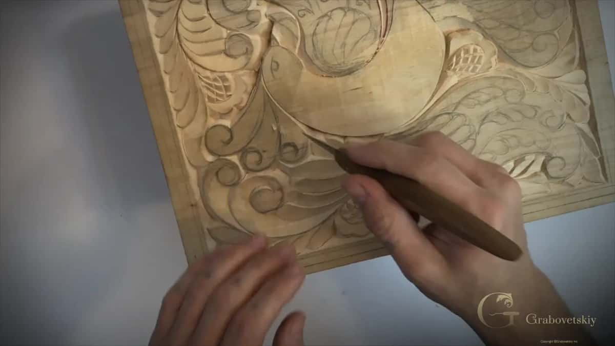 Carving along the lower curve of the bird with the small knife while the board sits at an angle
