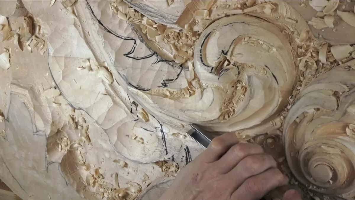The hand drops low and the blade points back up the leaf toward the curl.