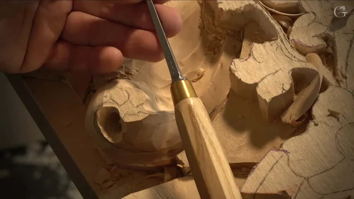 A gouge with a brass ferrule reaches down into the round hole below the leaf