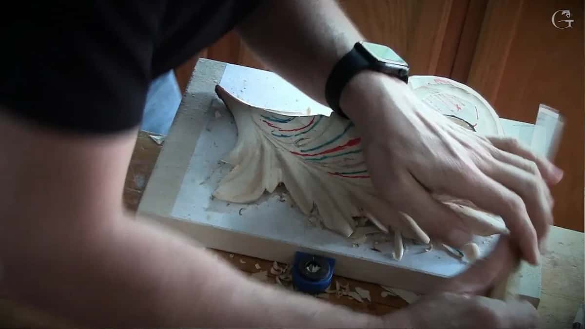 Two hands push a gouge through the lines