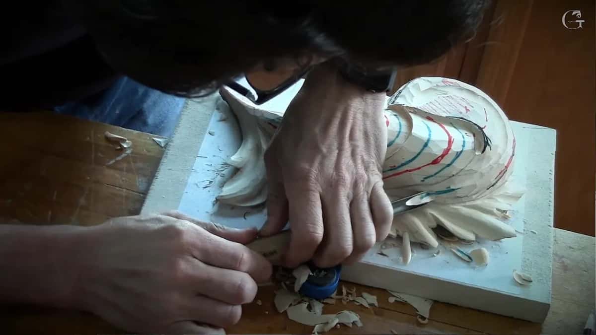 Close up, two hands guide a gouge through the drawn lines on the lobes