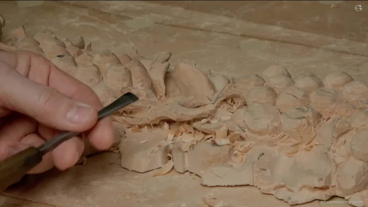 Seen low across the board, a dark-handled tool rests in the fingers with chips piled up behind it