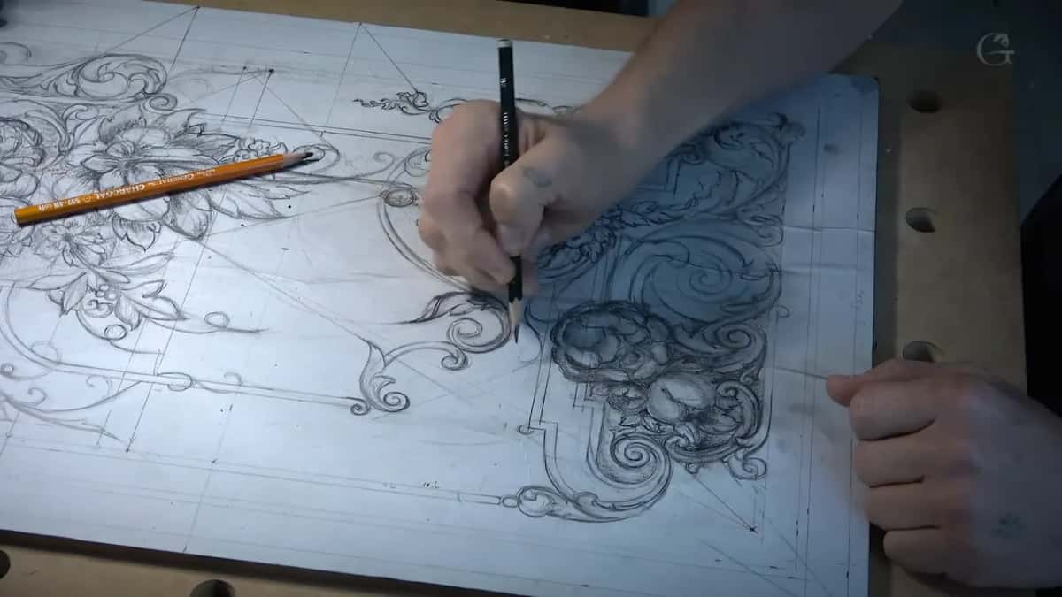Seen at a slant, a black pencil works over the dark scrolls while an orange one lies on the left