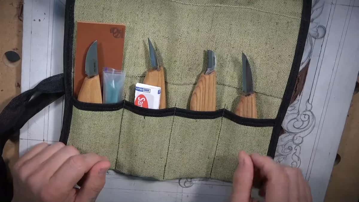 Four knives sitting in a canvas roll, a piece of leather at one end and a small packet tucked in the middle