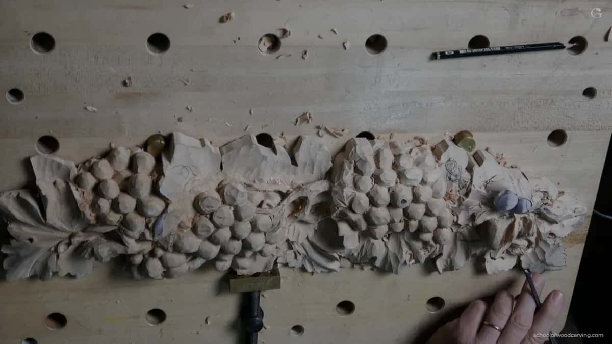 The grape panel flat on a bench full of round holes, a pencil lying above it and one hand working at the right end