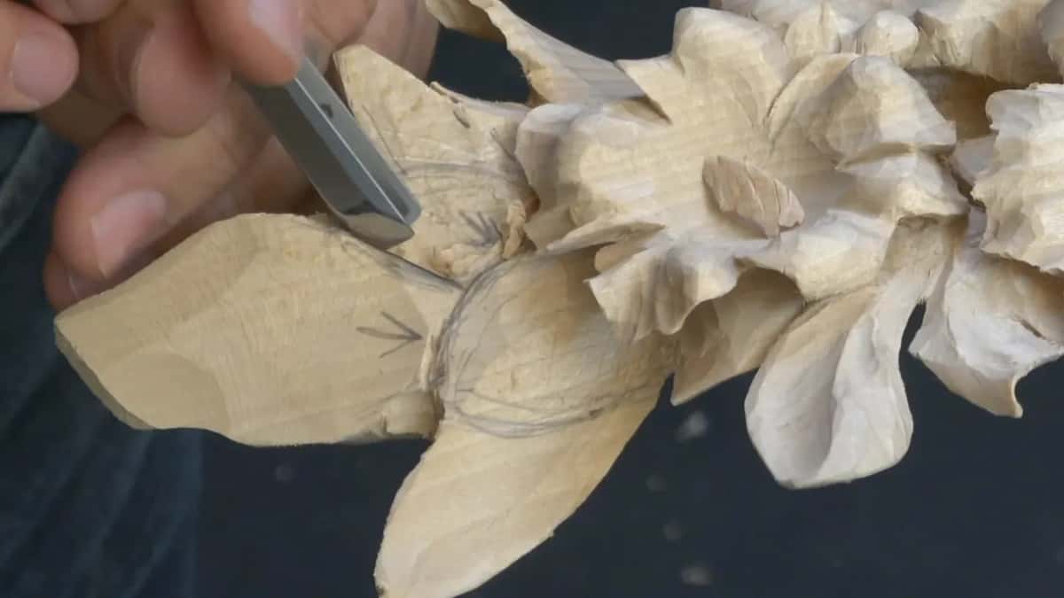 A straight tool sits on the pencil line where a new leaf meets a carved flower