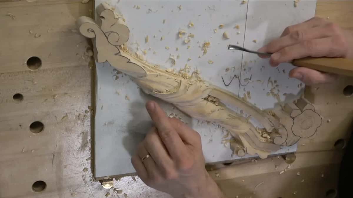 Left hand flat on the board while the right hand brings a small gouge in toward the leaf