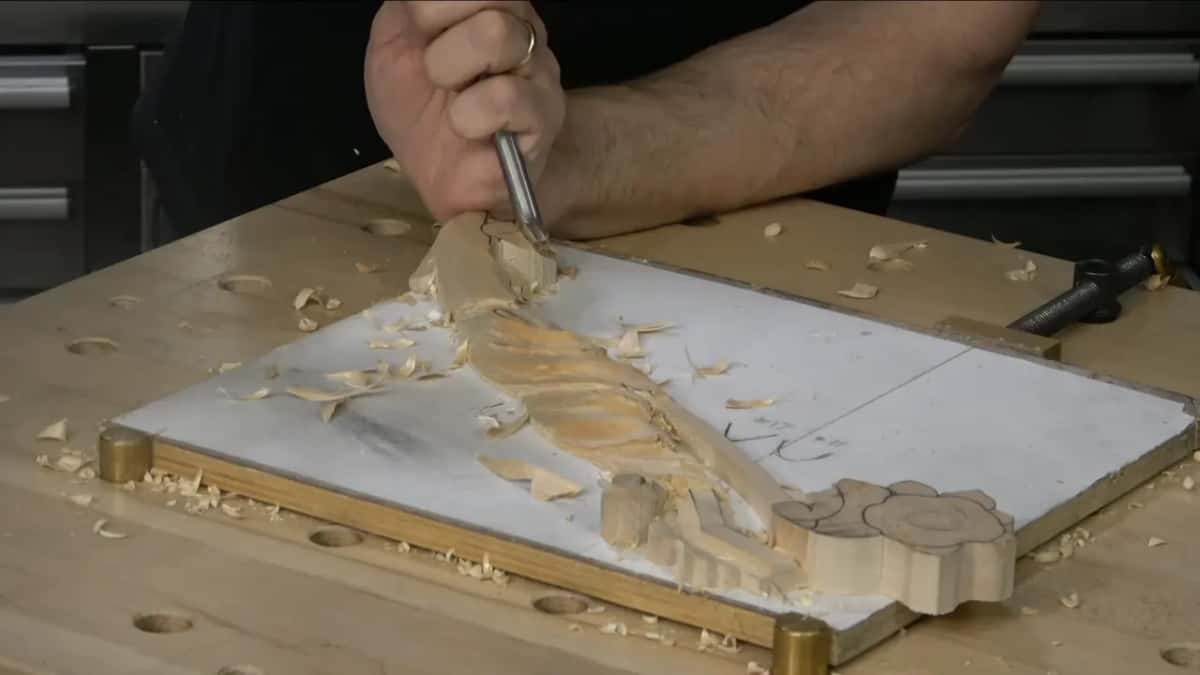 One hand pushes a gouge into the far end of the leaf, with the scroll waiting at the other end