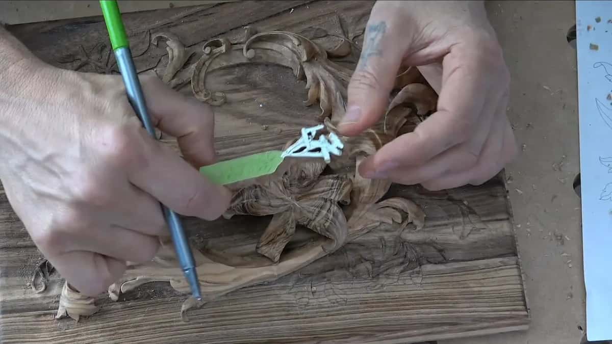 One hand holds a pen while the other keeps the sawn blank against the center of the carved flower.