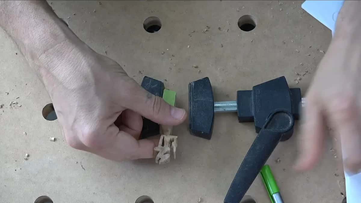 Fingers bring the green tab toward a bar clamp's open jaws.