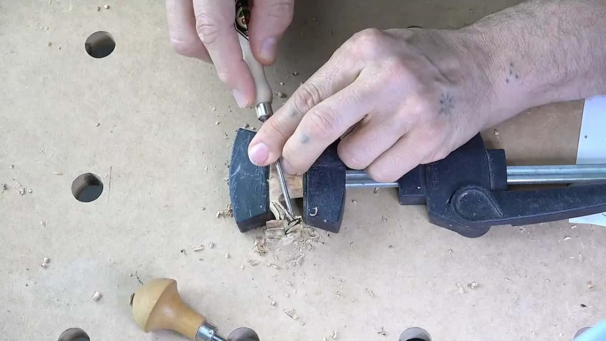 Both hands steady a small veiner in the clamped blank, a round-handled palm tool lying on the bench.