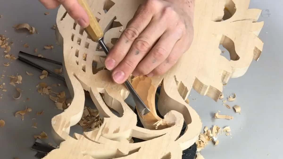One hand flat on the bare back while the other pushes a gouge in beside the square openings