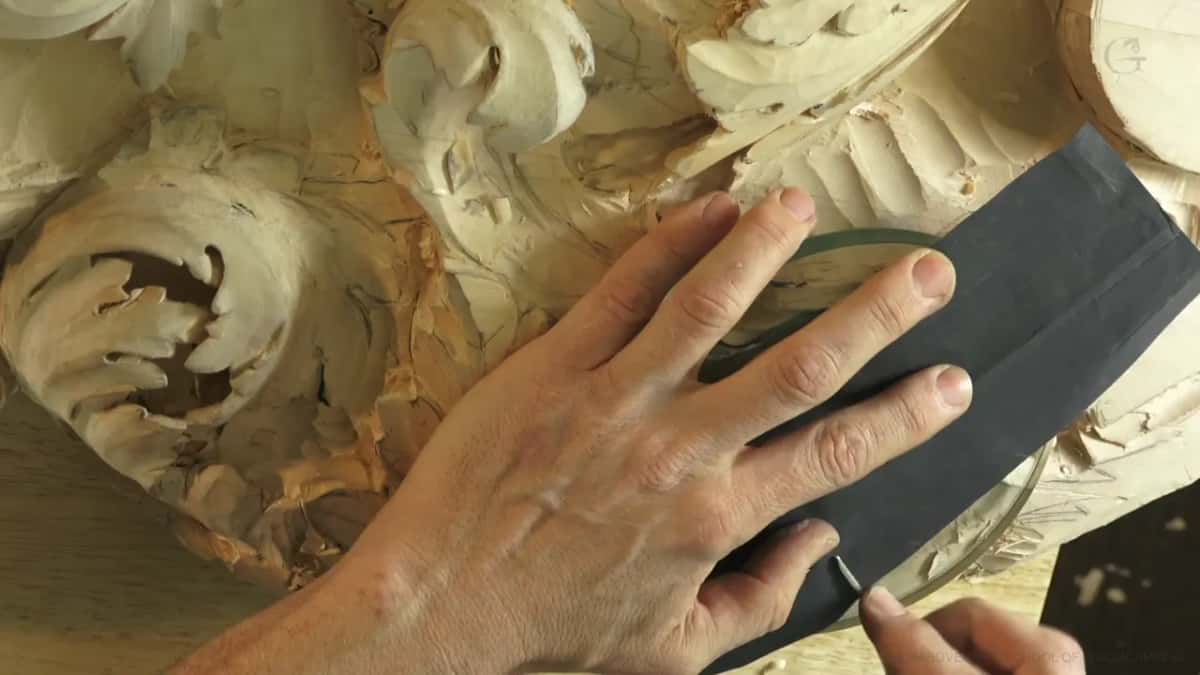 One hand pressing black sandpaper flat over a round plate, carved acanthus to the left