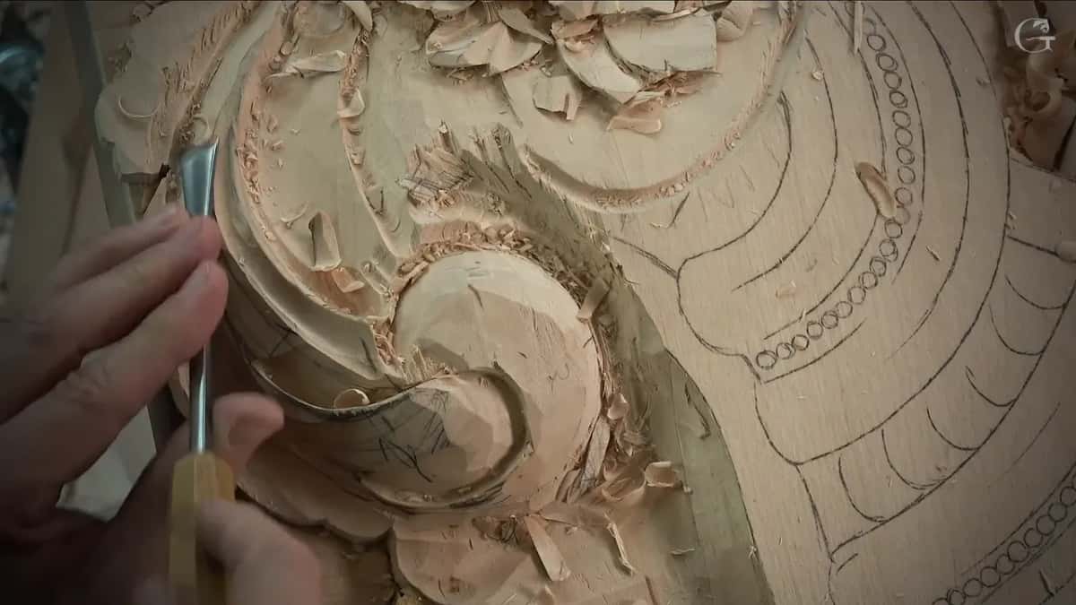 Fingers hold a small gouge upright at the rim of a curled scroll