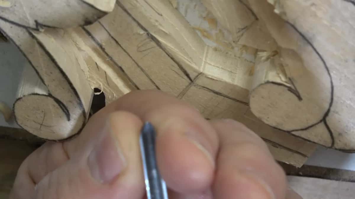 Thumb and finger pinch a narrow tool right beside the curled scroll of the molding.