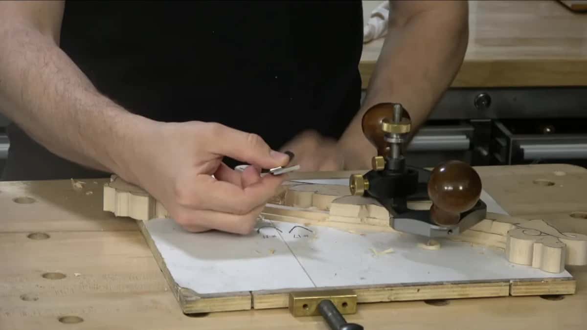 Small blade held between my fingers while the router plane sits on the carving beside it, ready.