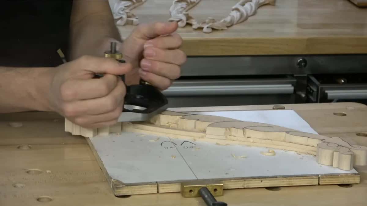 Router plane gripped on one side, resting on the carving.