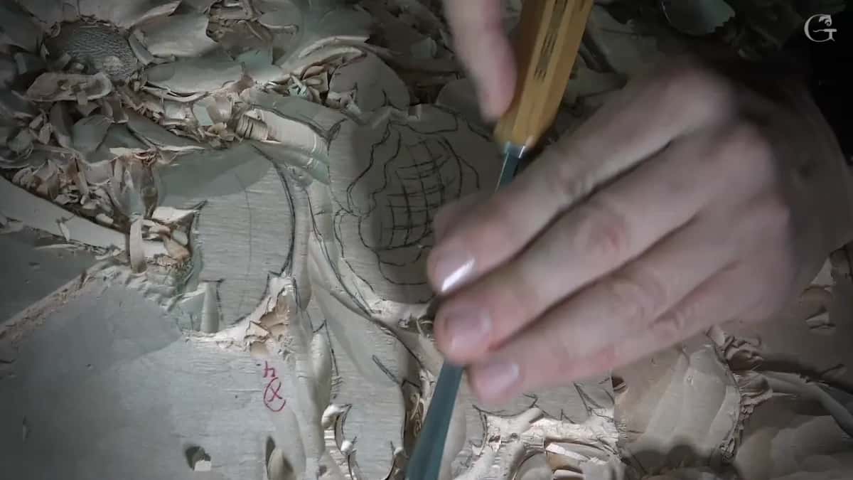 Steel pushed along a leaf edge beside the drawn flower, chips piled all around it