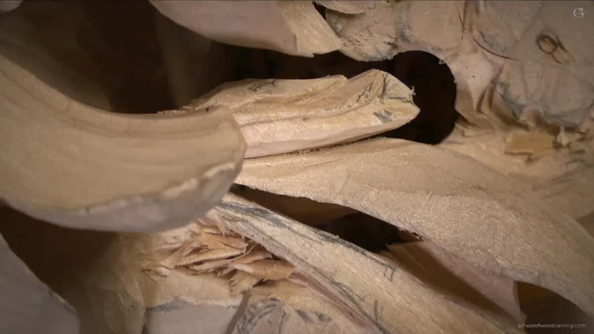 Close up, a black opening behind a curved carved leaf, pencil lines on the wood below it
