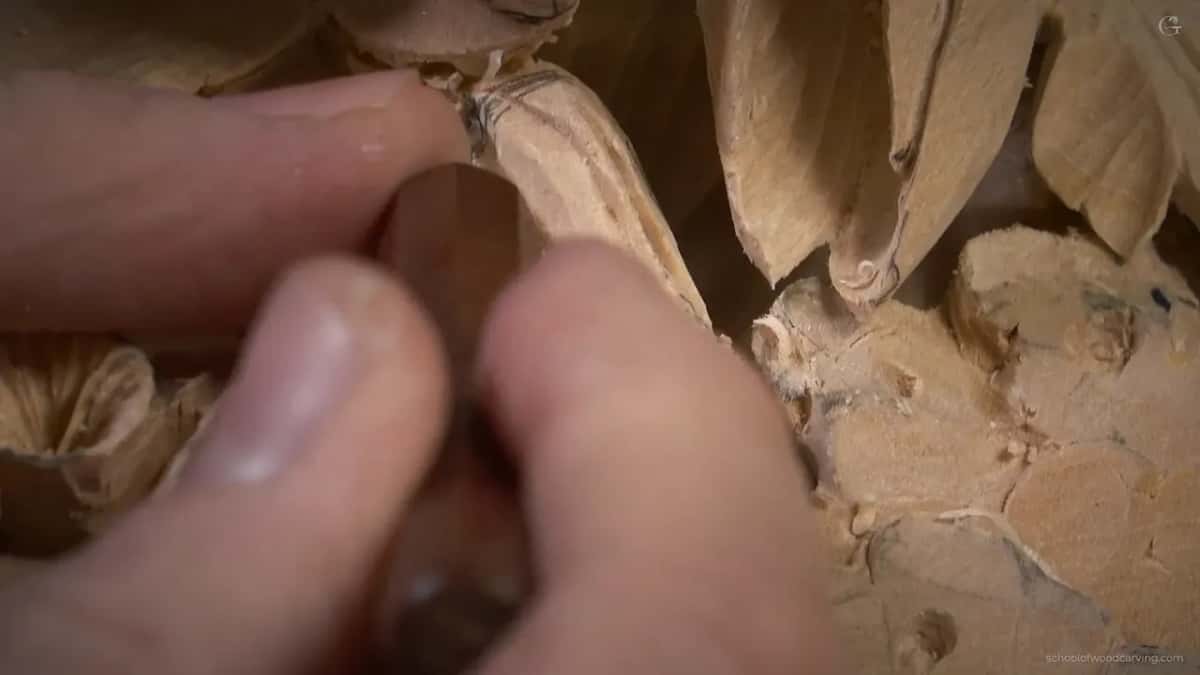 Two fingertips pinch a small brown handle low between the carved petals