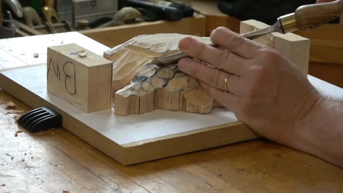 Wood handle held high, the other hand's fingers resting on the blade at the edge of the cluster
