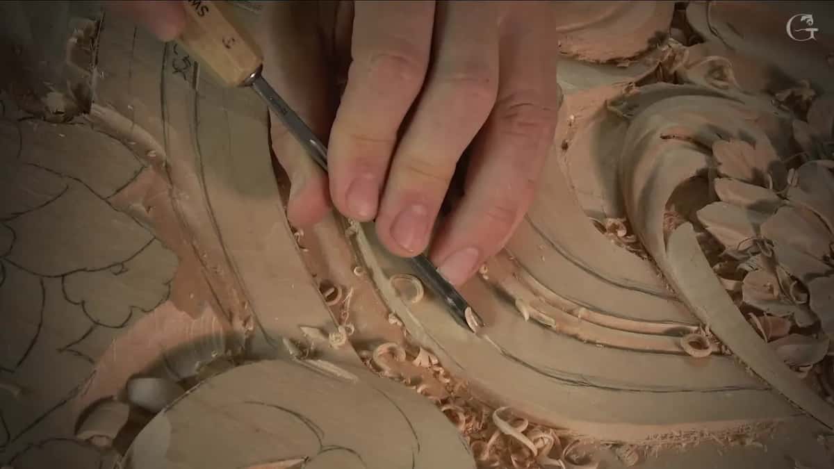 Gouge with a stamped handle follows a pencil line around the curve, fingers steadying the steel