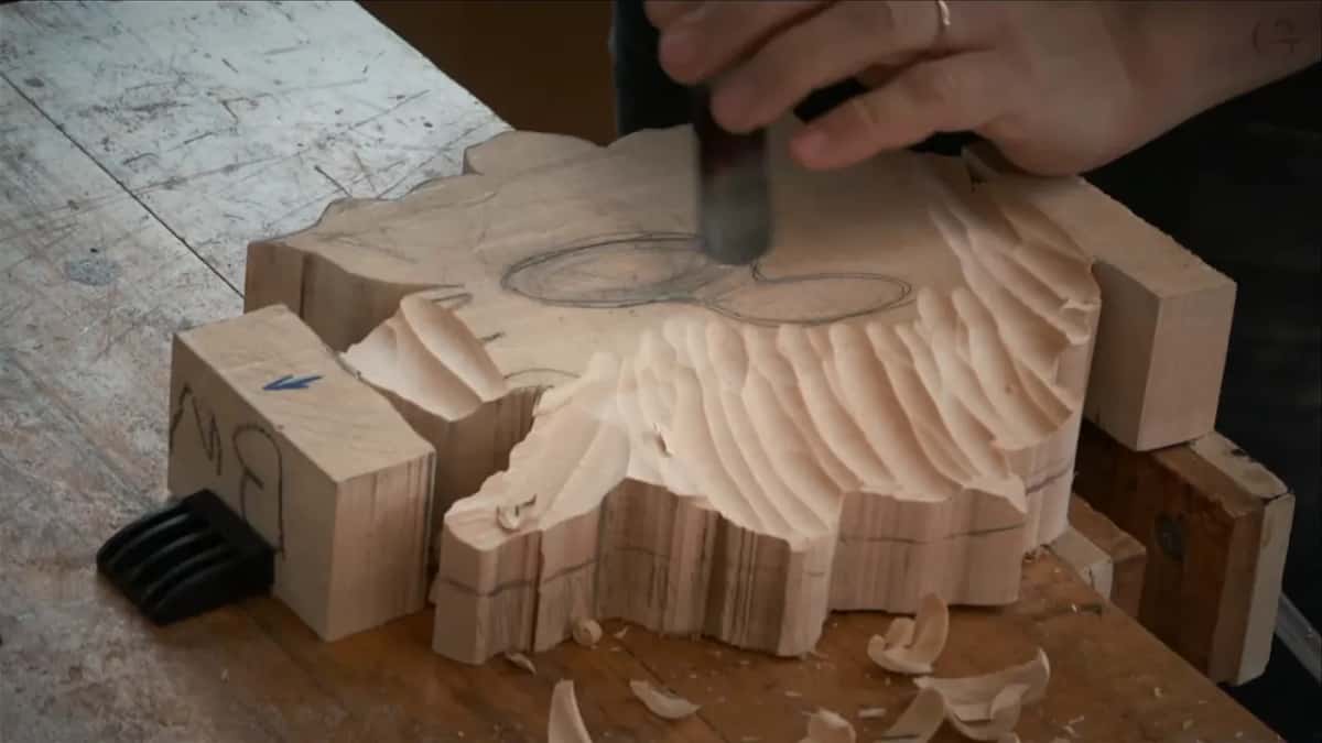 Gouge working through a broad band of facets while curled shavings drop onto the bench and pile beside the blank