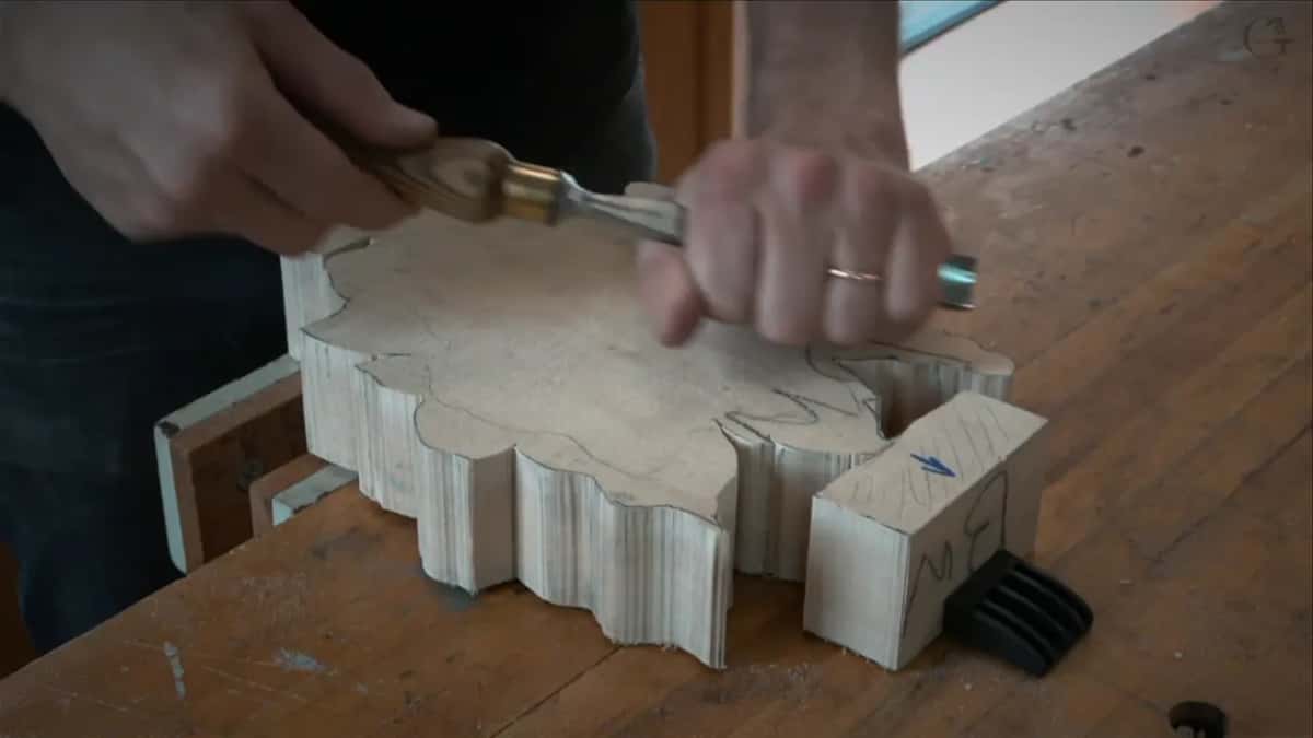 Both hands on a gouge, the guiding hand up near the blade, blank flat on the bench