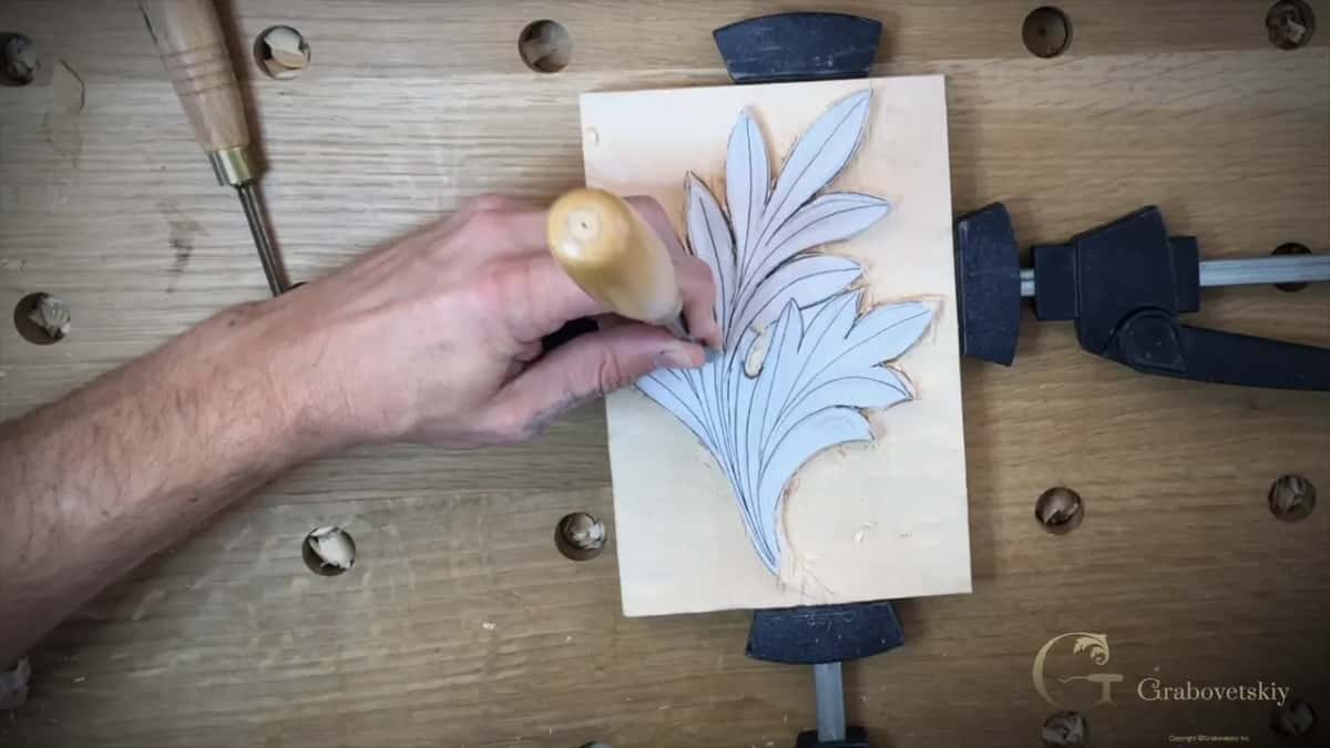 Palm on a pale handle over the leaf, another gouge lying on the bench behind