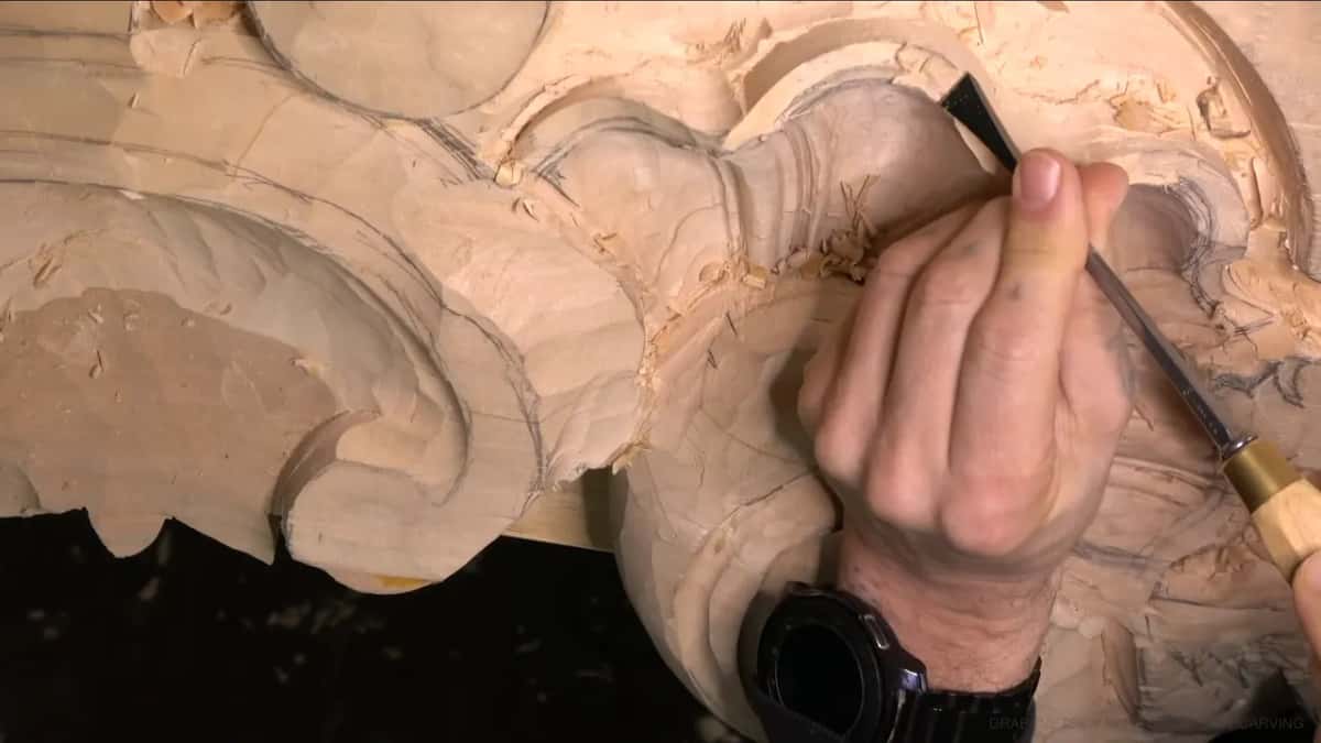 Held in one hand, a gouge smooths the top edge of the carved shell.