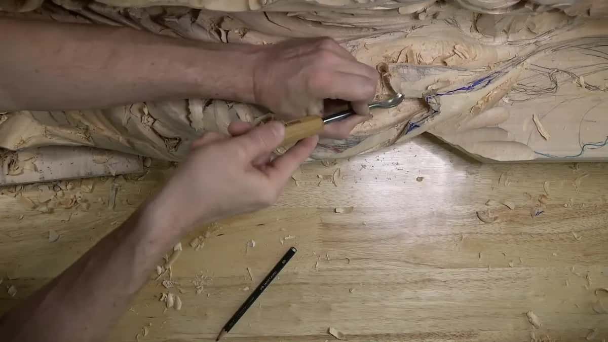 Curved spoon blade held in both hands, yellow handle angled up from the bench toward a hollow