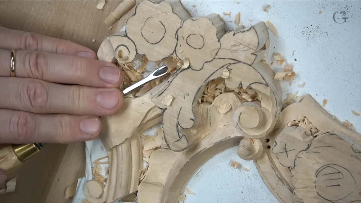 Fingers press a small gouge in beside a scroll under the pencil leaf