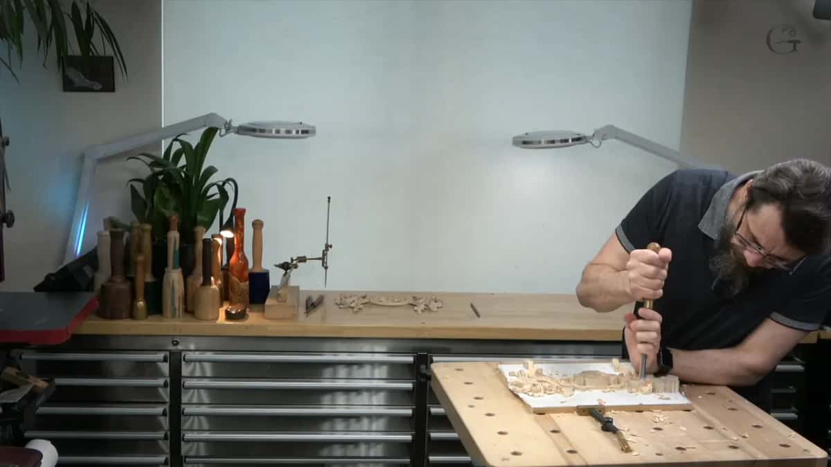 Leaning over the bench, both hands keep a tool upright in the wood