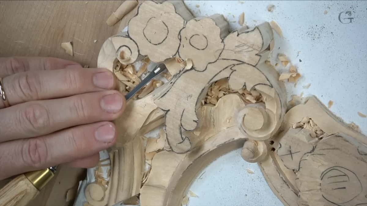 Fingertips guide a slim gouge between drawn flowers and a scroll