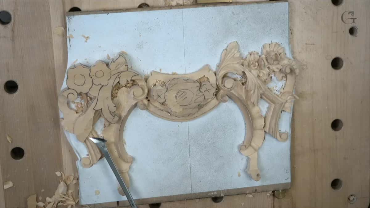 From above, a tool edge sits at the lower left scroll, the right half already carved