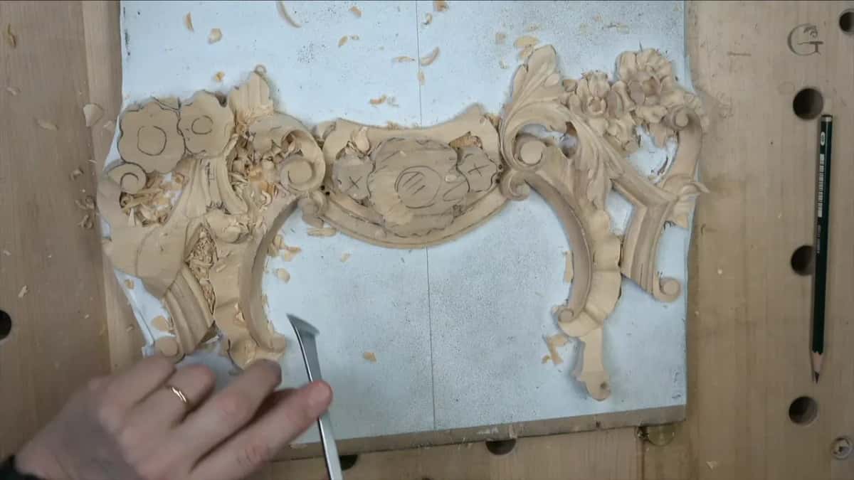 A hand brings a bent tool to the left end of the panel, a pencil lying on the board