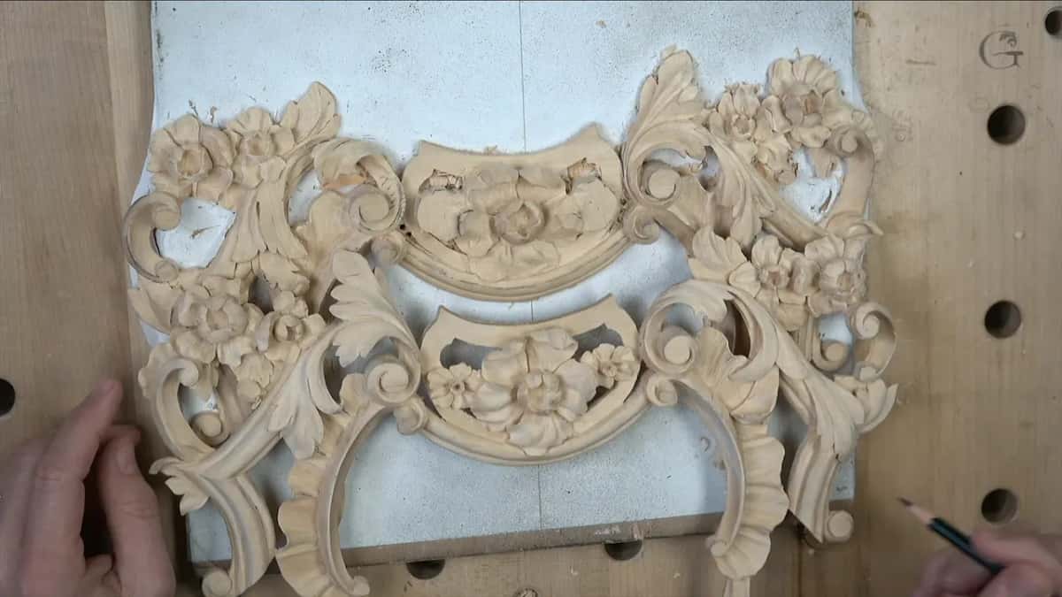 Upper and lower carved pieces laid together on the white board, a pencil at the lower right corner