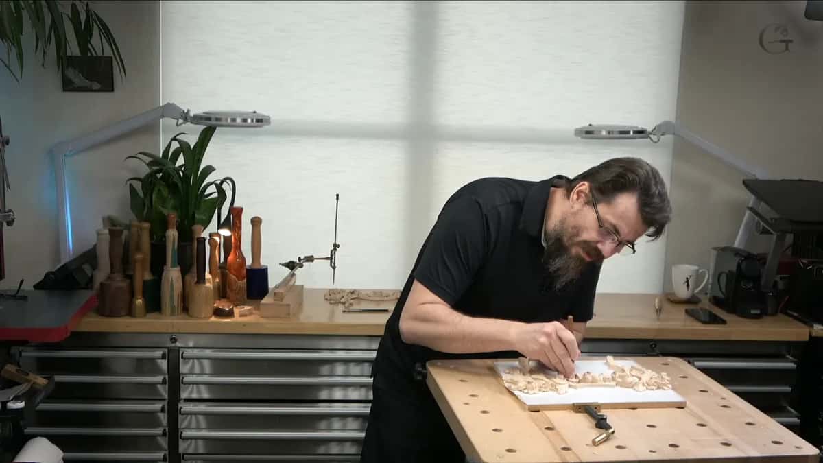 Bent low over the panel at the bench, two lamps on arms behind him