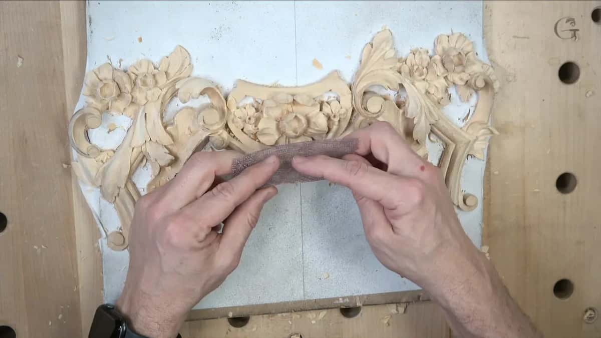 Both hands stretch sanding mesh over the carved panel