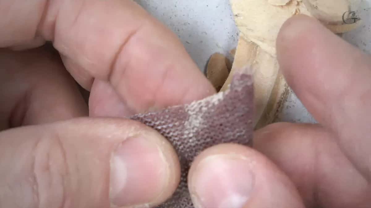 Fingertips hold a scrap of sanding mesh with pale dust in its holes