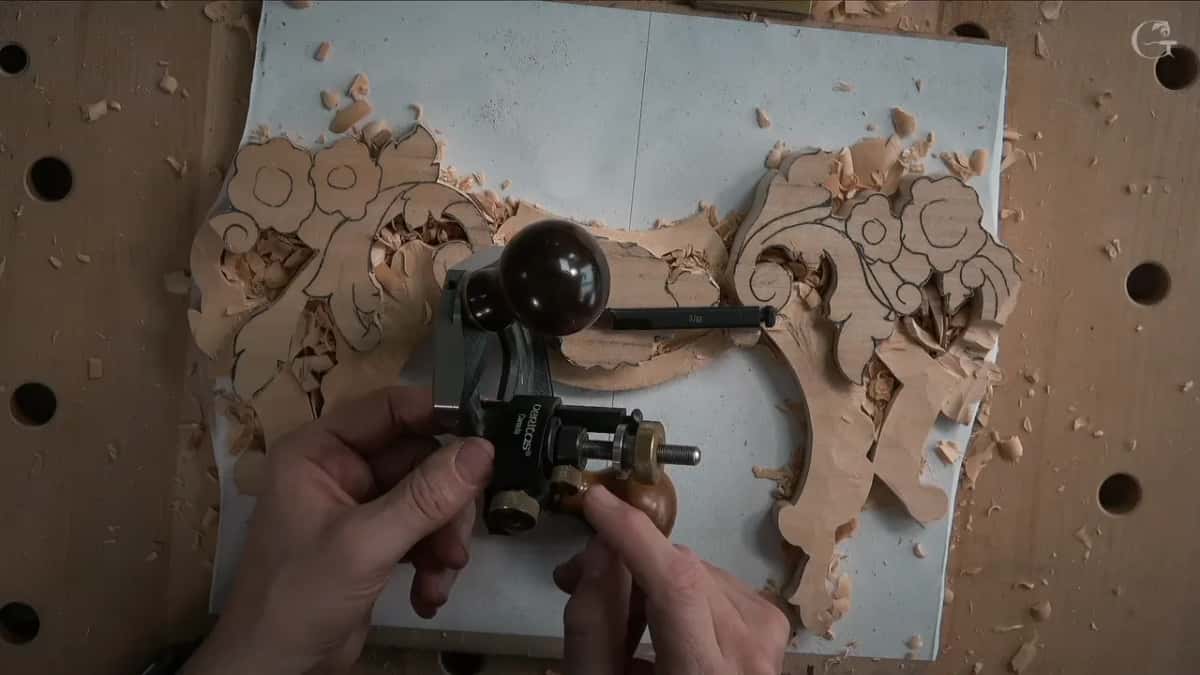 Both hands on a Veritas router plane above the carved panel