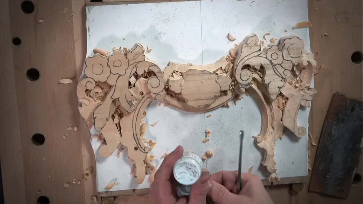 Open jar of white paste and a small gouge over the panel, a dark leather strip on the right