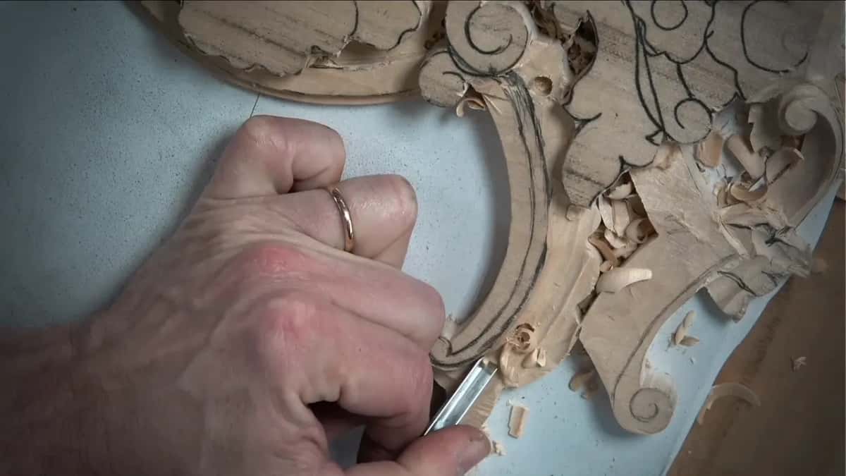 Small gouge in his fist, deep in the curved channel, fresh shavings piled along its edge