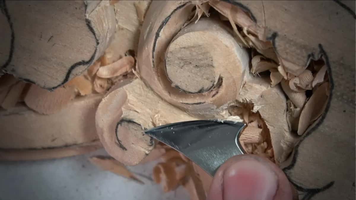 Knife-shaped blade slicing beside a carved scroll, thumb on the steel